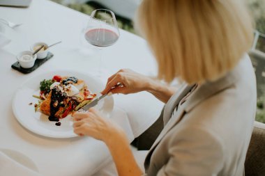 A person is savoring a carefully plated dish at a well-designed restaurant. The atmosphere is elegant, and a glass of red wine complements the meal, enhancing the dining experience.