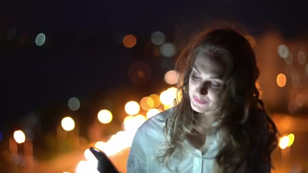 在夜景背景下使用智能手机 与街灯聊天或视频聊天的漂亮女人 — 图库视频影像