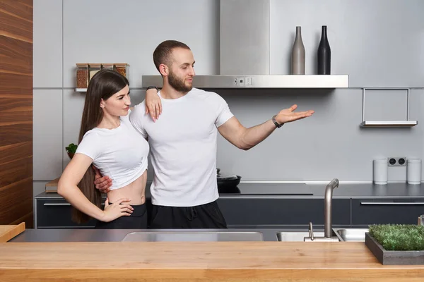 モダンなキッチンで若いカップル 彼は手のひらに空白のコピースペースを示す 製品を宣伝する — ストック写真