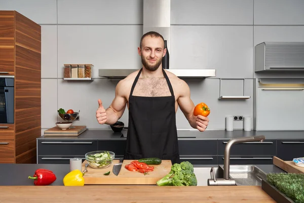 肌肉发达的男人宣传健康的蔬菜食品 在现代厨房里 穿着大厨围裙的肌肉男在做沙拉 — 图库照片