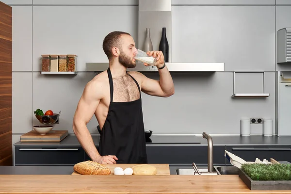Bezkoszulowy Muskularny Mężczyzna Noszący Fartuch Kucharski Pijący Mleko Stojące Nowoczesnej — Zdjęcie stockowe