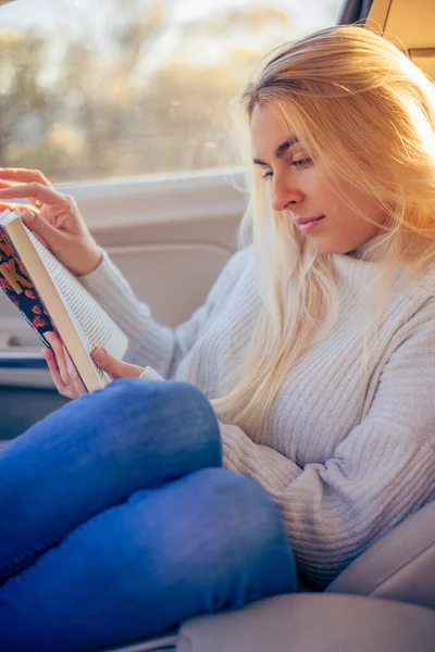 blonde woman read a book in the car on road trip