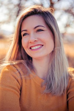 Sonbahar parkındaki mutlu kadın sarı kazağıyla gülümsüyor.