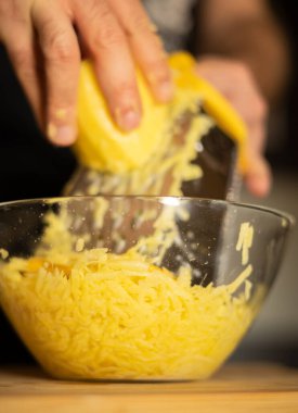 Ellerinde rende olan bir adam mutfakta patatesli gözleme yapmak için tahta tahtanın üzerindeki patatesleri cam kasede rendeleyecek. Sağlıklı beslenme ve yaşam tarzı.