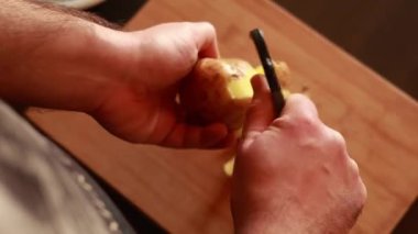 Erkeklerin elleri altın patatesi soyarken ve patates soyacağı ile sebzelerin derisini yüzerken.