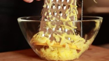 Ellerinde rende olan bir adam mutfakta patatesli gözleme yapmak için tahta tahtanın üzerindeki patatesleri cam kasede rendeleyecek. Sağlıklı beslenme ve yaşam tarzı.