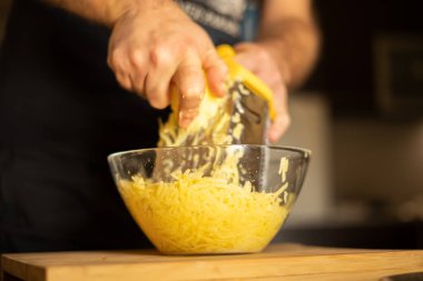 Ellerinde rende olan bir adam mutfakta patatesli gözleme yapmak için tahta tahtanın üzerindeki patatesleri cam kasede rendeleyecek. Sağlıklı beslenme ve yaşam tarzı.