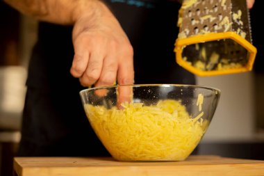 Ellerinde rende olan bir adam mutfakta patatesli gözleme yapmak için tahta tahtanın üzerindeki patatesleri cam kasede rendeleyecek. Sağlıklı beslenme ve yaşam tarzı.