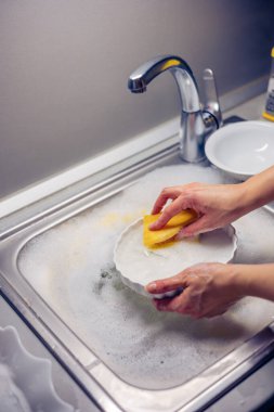 Kadın ev hanımı bulaşıkları yıkama süngeri ve bulaşık makinesiyle yıkıyor.