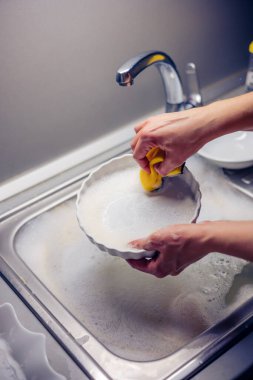 Kadın ev hanımı bulaşıkları yıkama süngeri ve bulaşık makinesiyle yıkıyor.