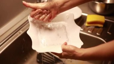 Kadın ev hanımı bulaşıkları yıkama süngeri ve bulaşık makinesiyle yıkıyor.