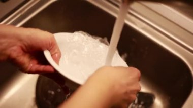 Kadın ev hanımı bulaşıkları yıkama süngeri ve bulaşık makinesiyle yıkıyor.
