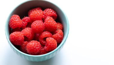 Ahududulu küçük mavi kase beyaz arkaplanı kaplıyor.