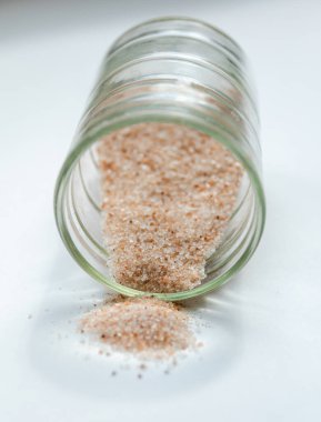 Beyaz arka plandaki küçük cam kaptan pembe tuz dökülmüş.