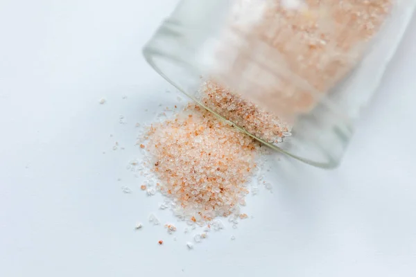 pink salt spill from small glass container on white background