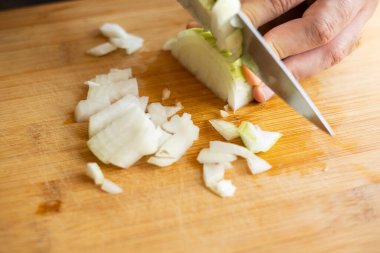 Adam elleri ev mutfağında ahşap tahtada soğan kesiyor.