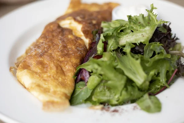 close up of a omelet with a side salad on a white plate