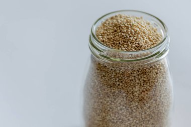 Cam bir kavanozdaki çiğ beyaz kinoa. Beyaz arka plana yakın.