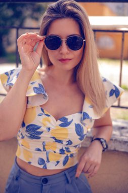 Güneş gözlüklü kadın dışarıda şık yazlık kıyafetler giyiyor.