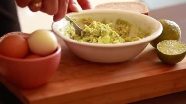 Kadın elleri avokado tostu için beyaz bir kâsede avokado ezer ya da evde guacamole yapar.