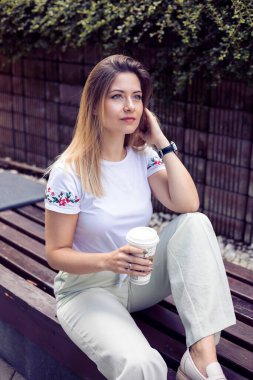 Sıradan giyinmiş bir kadını yakalayan, dışarı çıkıp kahvesini yudumlayan, günlük hayatın basit zevklerini özetleyen samimi bir görüntü.