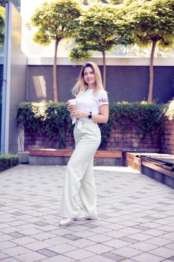 Sıradan giyinmiş bir kadını yakalayan, dışarı çıkıp kahvesini yudumlayan, günlük hayatın basit zevklerini özetleyen samimi bir görüntü.