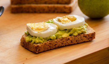  Üzerine mükemmel haşlanmış yumurta konmuş avokado tostu, sade ahşap bir tahtanın üzerinde sunuluyor.
