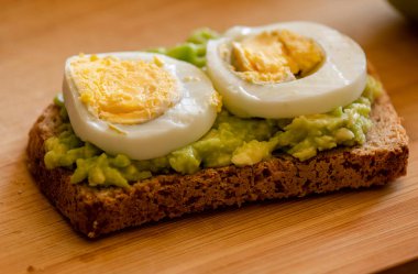  Üzerine mükemmel haşlanmış yumurta konmuş avokado tostu, sade ahşap bir tahtanın üzerinde sunuluyor.