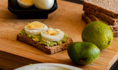  Üzerine mükemmel haşlanmış yumurta konmuş avokado tostu, sade ahşap bir tahtanın üzerinde sunuluyor.