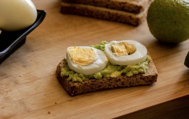  Üzerine mükemmel haşlanmış yumurta konmuş avokado tostu, sade ahşap bir tahtanın üzerinde sunuluyor.