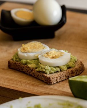  Üzerine mükemmel haşlanmış yumurta konmuş avokado tostu, sade ahşap bir tahtanın üzerinde sunuluyor.