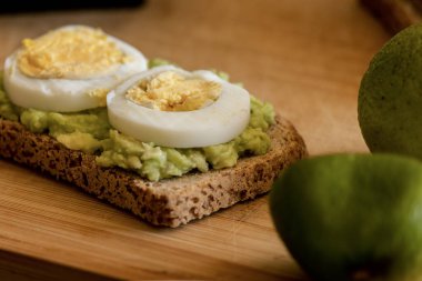  Üzerine mükemmel haşlanmış yumurta konmuş avokado tostu, sade ahşap bir tahtanın üzerinde sunuluyor.