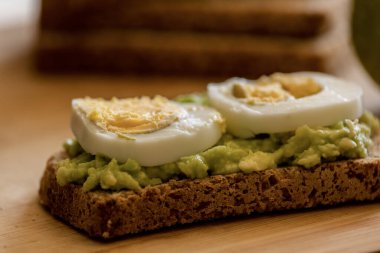  Üzerine mükemmel haşlanmış yumurta konmuş avokado tostu, sade ahşap bir tahtanın üzerinde sunuluyor.