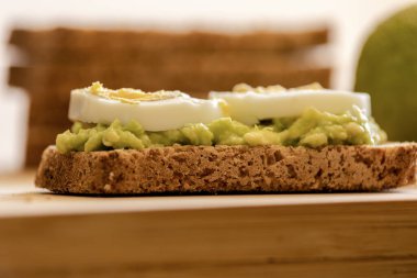  Üzerine mükemmel haşlanmış yumurta konmuş avokado tostu, sade ahşap bir tahtanın üzerinde sunuluyor.