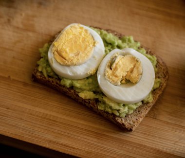  Üzerine mükemmel haşlanmış yumurta konmuş avokado tostu, sade ahşap bir tahtanın üzerinde sunuluyor.