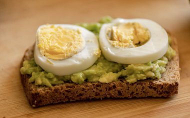  Üzerine mükemmel haşlanmış yumurta konmuş avokado tostu, sade ahşap bir tahtanın üzerinde sunuluyor.
