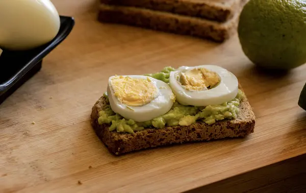  Üzerine mükemmel haşlanmış yumurta konmuş avokado tostu, sade ahşap bir tahtanın üzerinde sunuluyor.