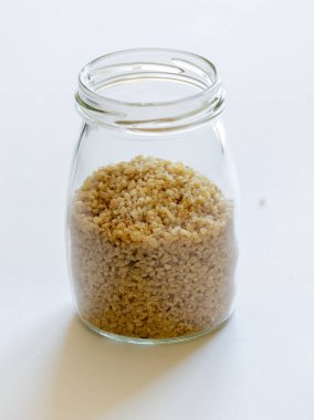 Bulgur tanecikleri cam kavanozda temiz beyaz bir arkaplana karşı güzelce depolanmış.
