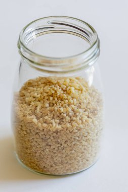 Bulgur tanecikleri cam kavanozda temiz beyaz bir arkaplana karşı güzelce depolanmış.