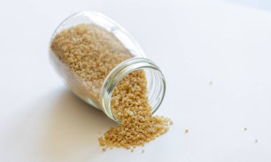 Bulgur tanecikleri cam kavanozda temiz beyaz bir arkaplana karşı güzelce depolanmış.