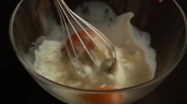 Krep için sıvı malzemeleri çırpıcı ile karıştırıyorum. Mutfak masasının üst manzarası. Mutfakta yemek pişirmek.