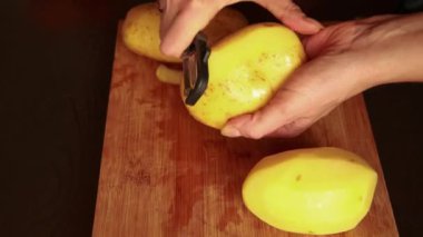 Patates soyan eller. Kadın patates soyacağı ile patates soyuyor. Patates yemek pişirmek için hazırlanıyor. Yakın plan.