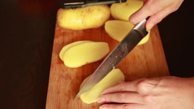 Patates kesmek. Bıçağı kapat, patatesi kes. sebze pişirmek. Yemek hazırlama. Kadın taze patates keser. Ahşap mutfak tahtasının üzerinde olgun patates kesikleriyle kadın eli
