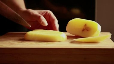 Patates kesmek. Bıçağı kapat, patatesi kes. sebze pişirmek. Yemek hazırlama. Kadın taze patates keser. Ahşap mutfak tahtasının üzerinde olgun patates kesikleriyle kadın eli