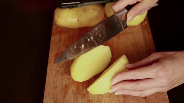 ジャガイモを切る ナイフカットジャガイモを閉じろ 野菜を調理する 食べ物の準備について 女性は新鮮なジャガイモをカットします 木製のキッチンボードにカット熟したジャガイモを付ける女性の手 — ストック動画