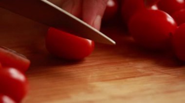 Kadın elleri kiraz domateslerini ahşap tahtada ortadan kesiyor.