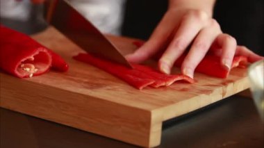 Mutfak inceliği: kadın elleri tahta tahtada taze kırmızı dolma biber kesiyor.