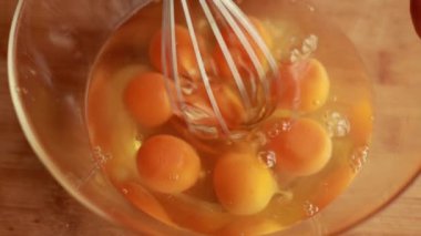 Büyük bir cam kasede büyük miktarda yumurtayı karıştırırken yakın plan çekimler.