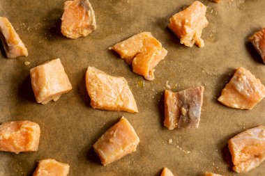 Çiğ somon filetolarının yakın plan çekimi küp şeklinde kesilmiş ve bir tepside parşömen kağıdına dizilmiş, pişirmeye, kalitelerini ve tazeliklerini sergilemeye hazır.