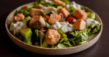 Lezzetli bir Akdeniz salatasına yakın plan. İçinde somon filetosu ve bir tutam tzatziki sosu var. Taze ve lezzetli bir yemek deneyimi sunuyor.